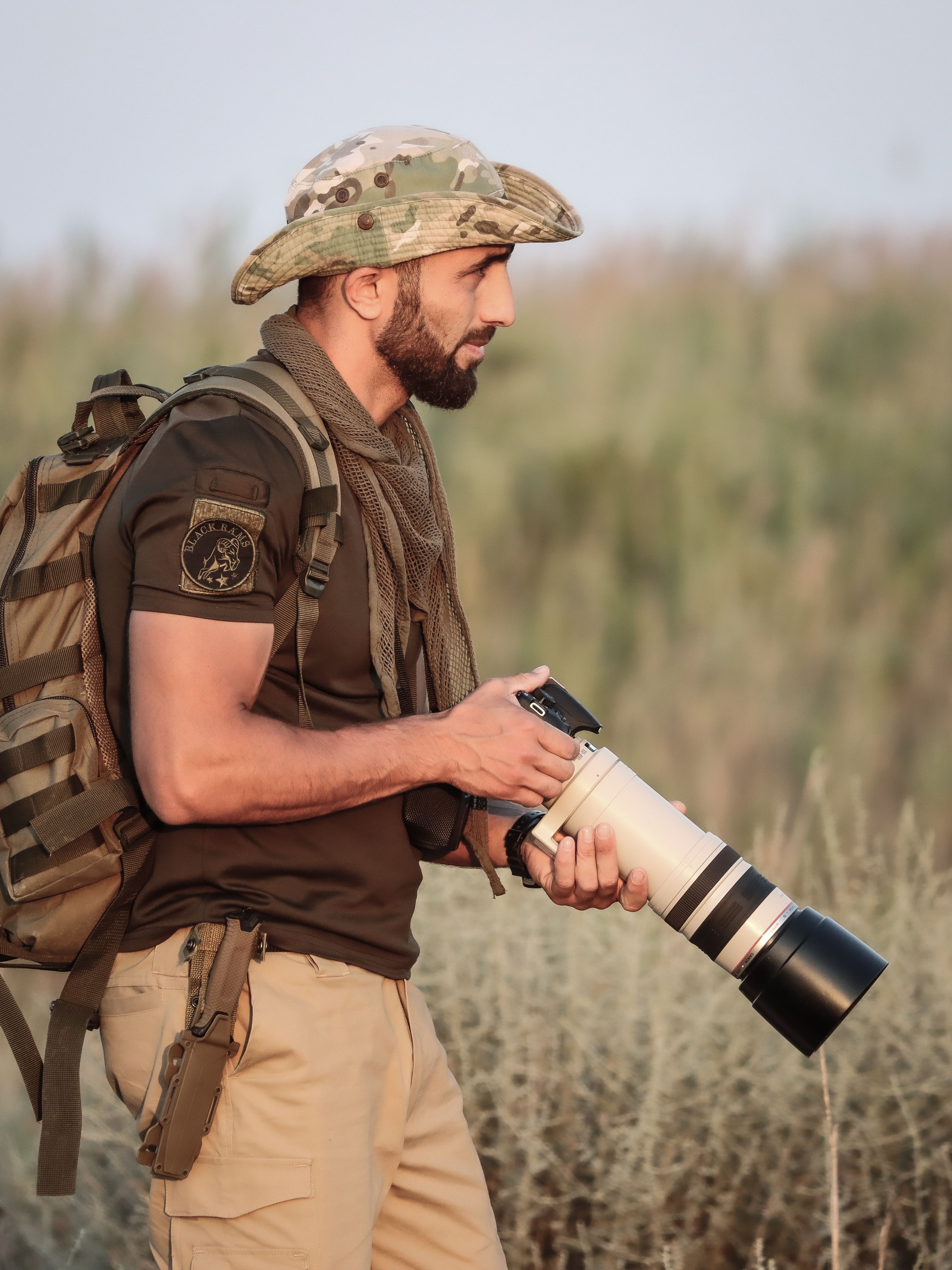 A man in camouflage attire with a telephoto lens camera outdoors, capturing nature.