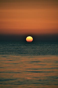 Sun setting over calm ocean waters with vibrant orange and blue hues, perfect for relaxation themes.