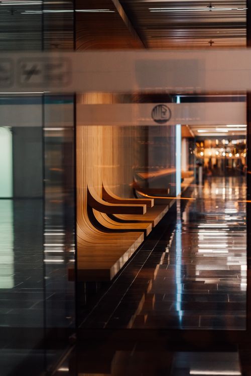Free A sleek, modern hallway featuring glass walls and wooden seating, captured in warm lighting. Stock Photo