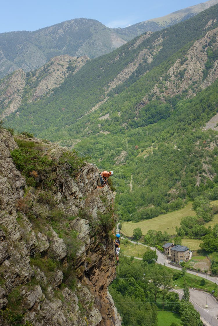 People Climbing On A Steep Cliff Over A Mountain Valley