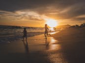 轮廓上的孩子们在充满活力的日落中在风景优美的海滩上快乐地玩耍