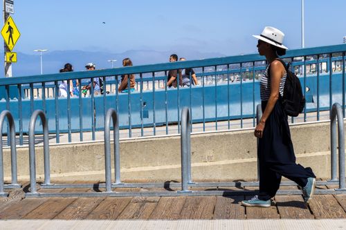 Free A woman in a white hat and backpack walks along an urban walkway on a sunny day. Stock Photo