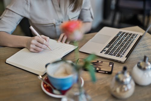 Free Person Writing On A Notebook Beside Macbook  Stock Photo