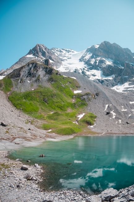 Stunning mountain lake with clear reflections and snowy peaks under a bright sky.