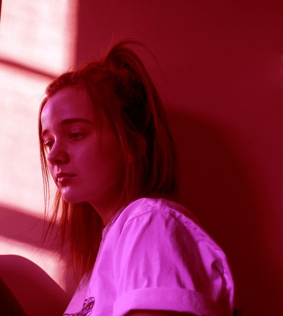 A young woman in a moody, red-lit environment, sitting indoors. Captured with a Canon DSLR.