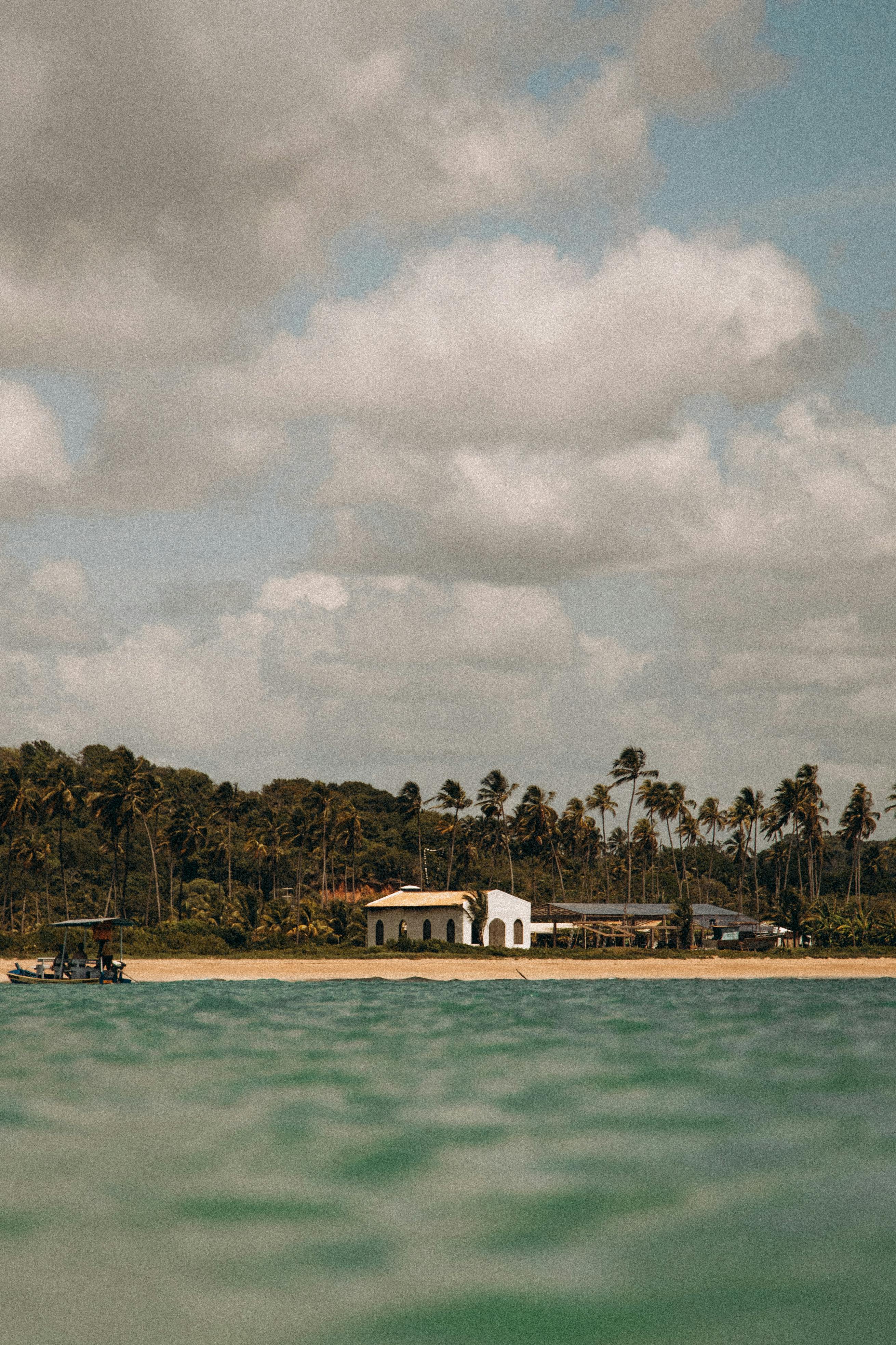 Tranquil beach scene with chapel in São Miguel dos Milagres, Brazil, under a cloudy sky.
