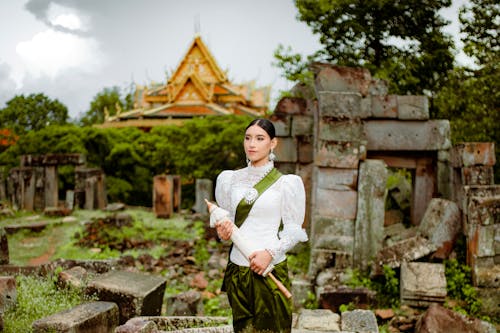 Model in a White Chiffon Embroidered Blouse with a Green Sash and a Green Silk Printed Sampot Skirt Holding an Umbrella Posing in Ruins of A Temple