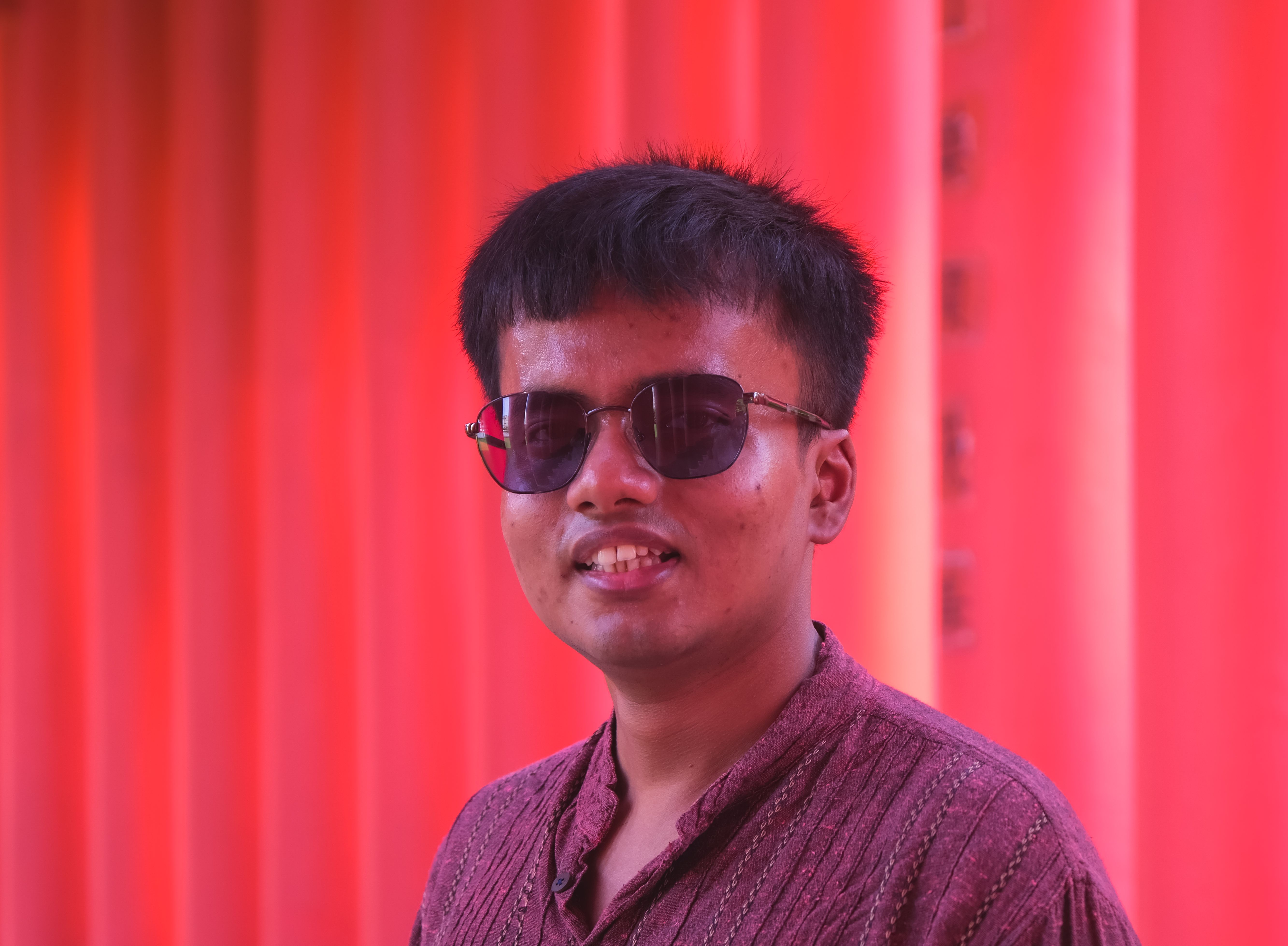Portrait of a smiling man with sunglasses against a red backdrop, exuding style.