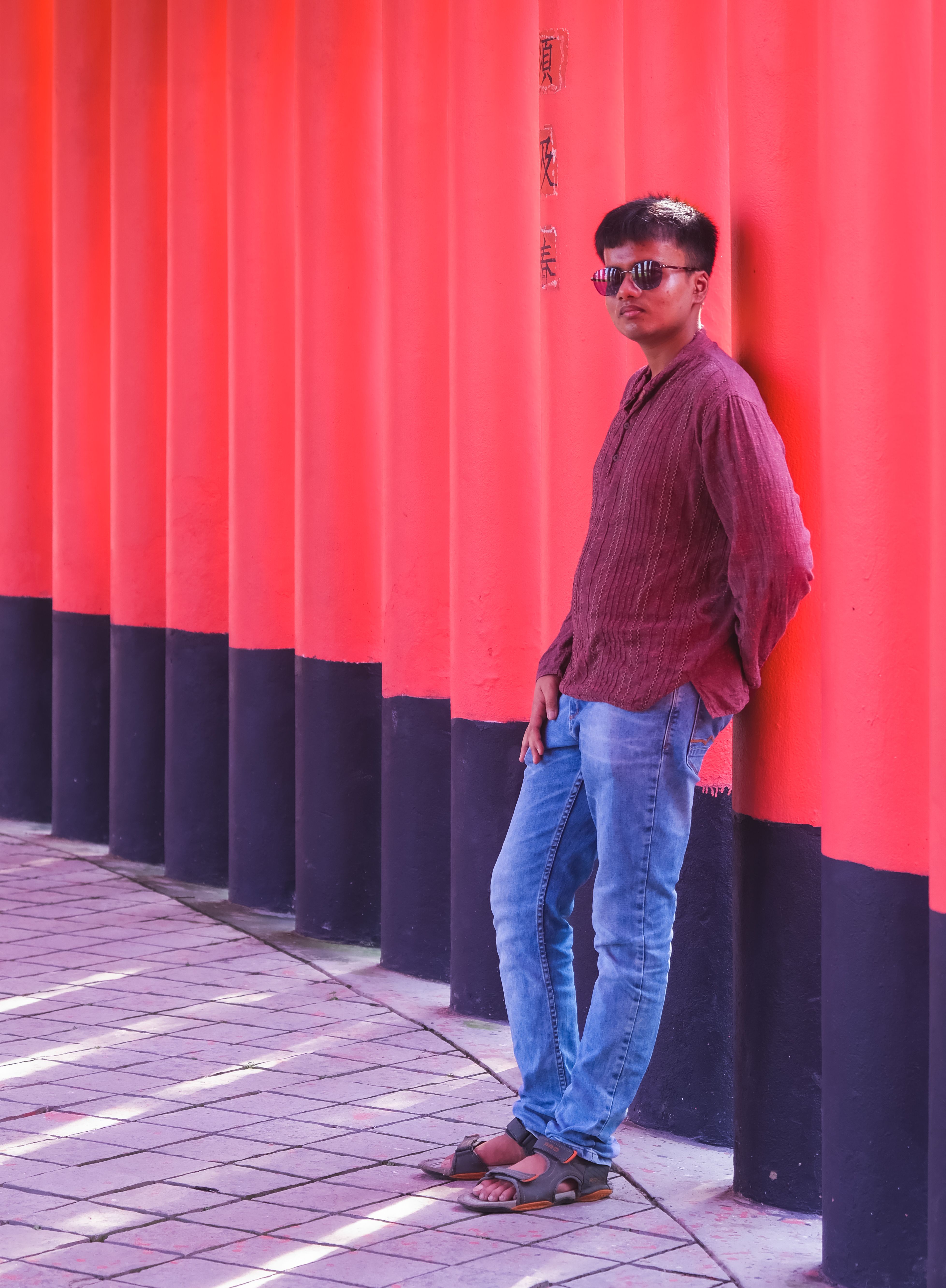 Man leaning against red torii gates, casual and stylish pose outdoors.