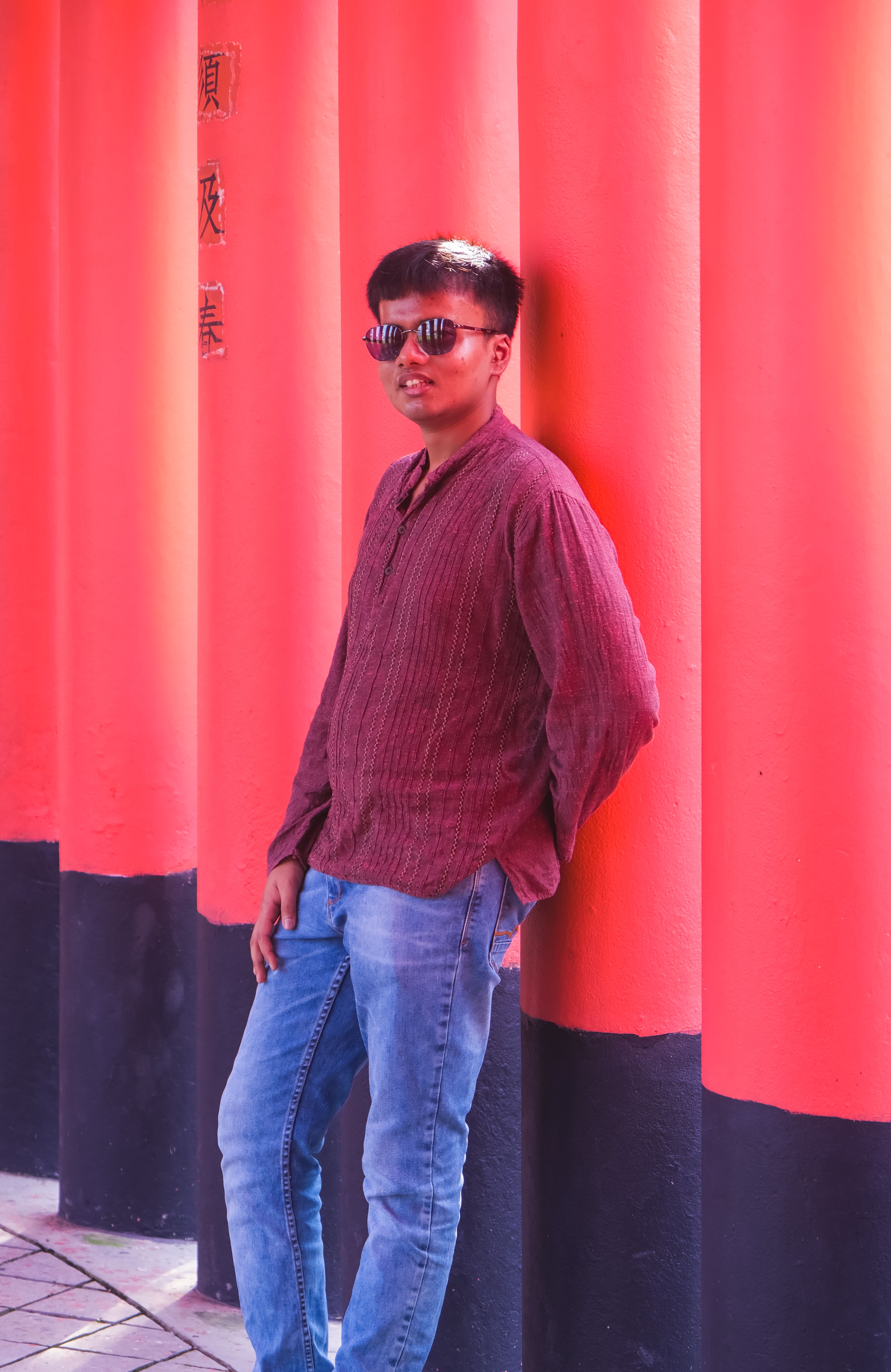 Young man in sunglasses leans on colorful pillars, embracing a casual vibe.