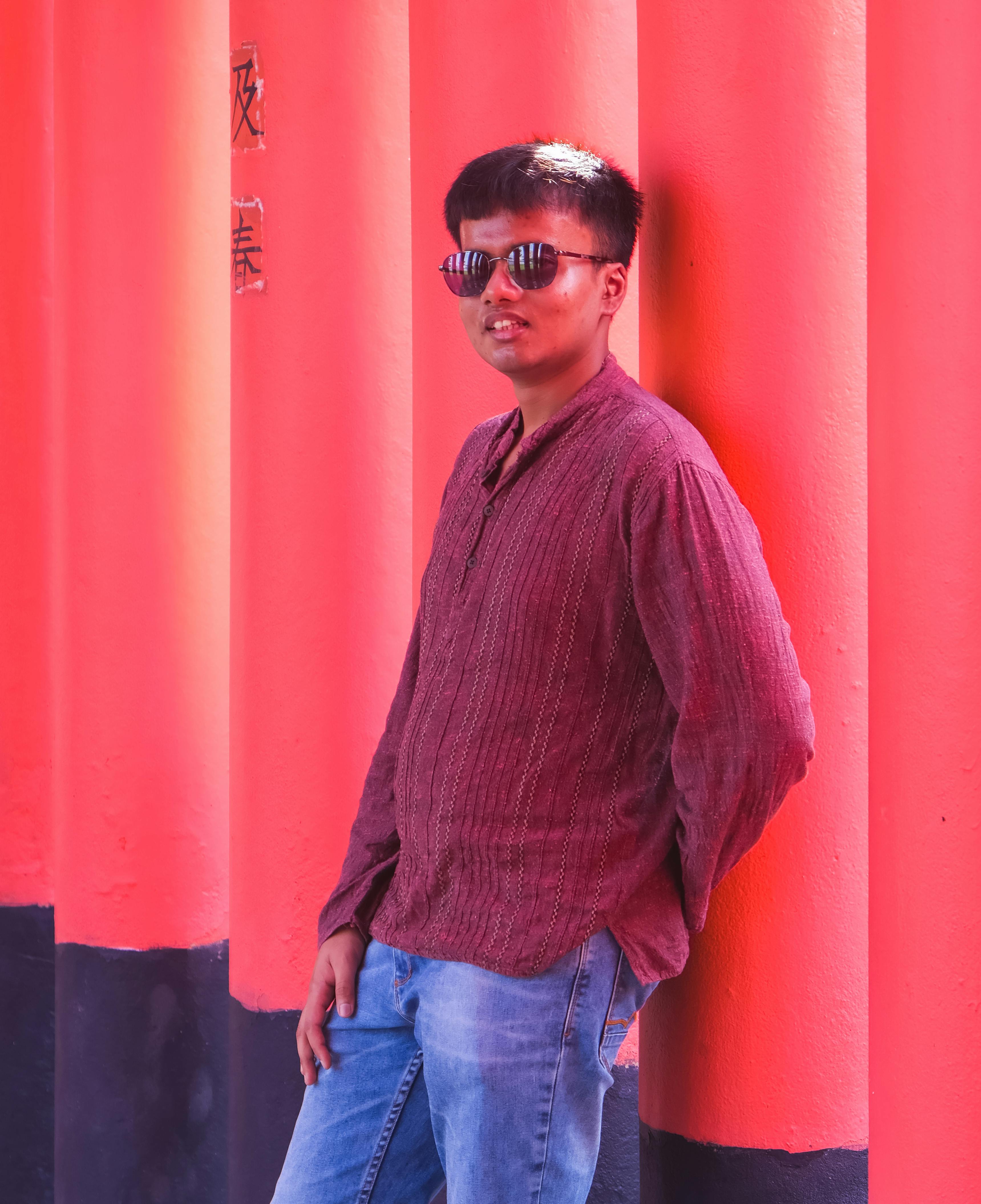 Stylish man in sunglasses leaning against red columns in a casual pose outdoors.
