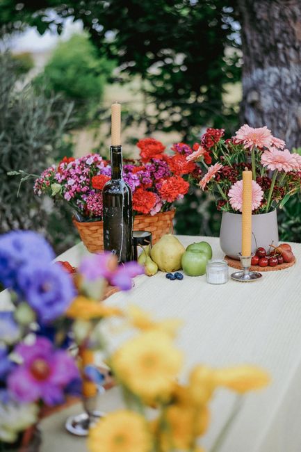 Vibrant summer outdoor table with flowers, fruits, and wine in a rustic setting.