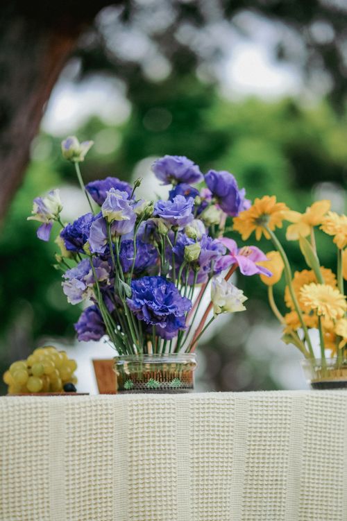 Free Vibrant arrangement of purple and yellow flowers in glass vases on a textured table outdoors. Stock Photo