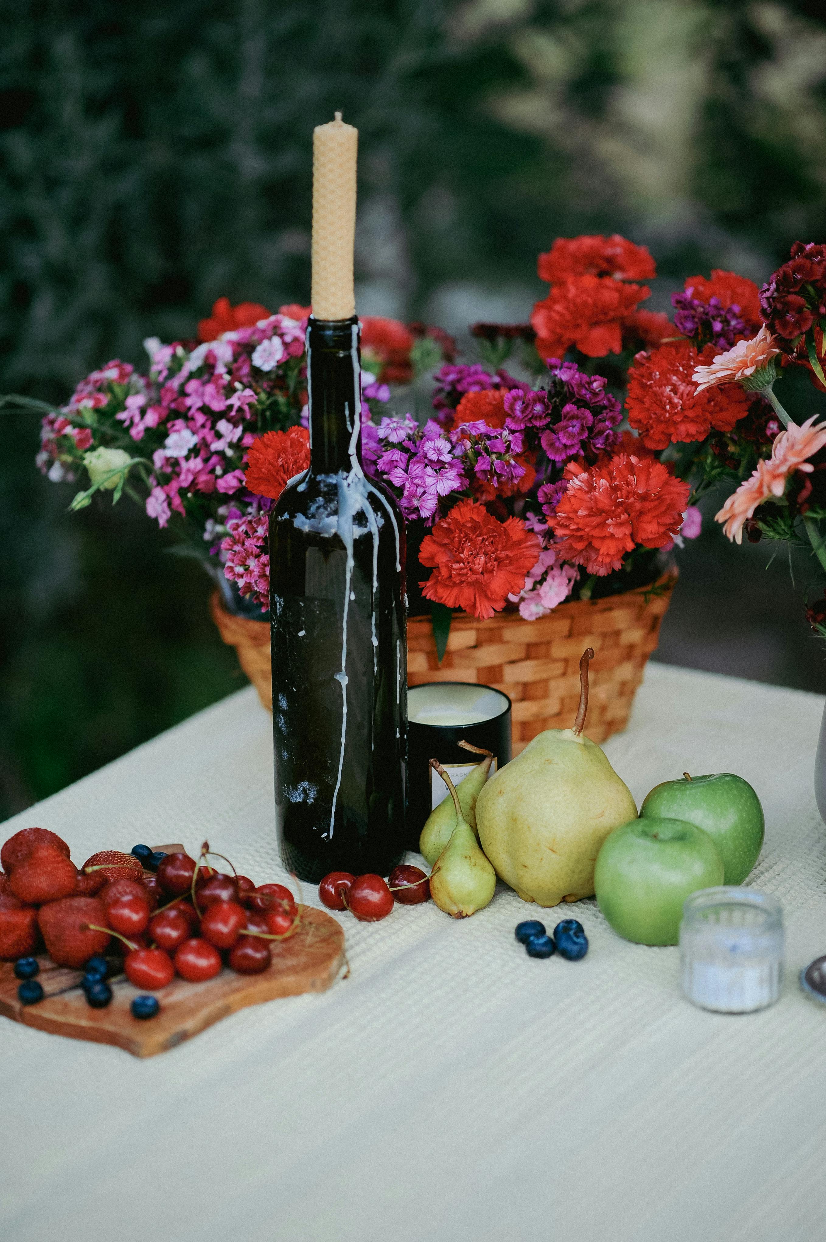 Colorful floral arrangement with fruits and candle on a table outdoors.