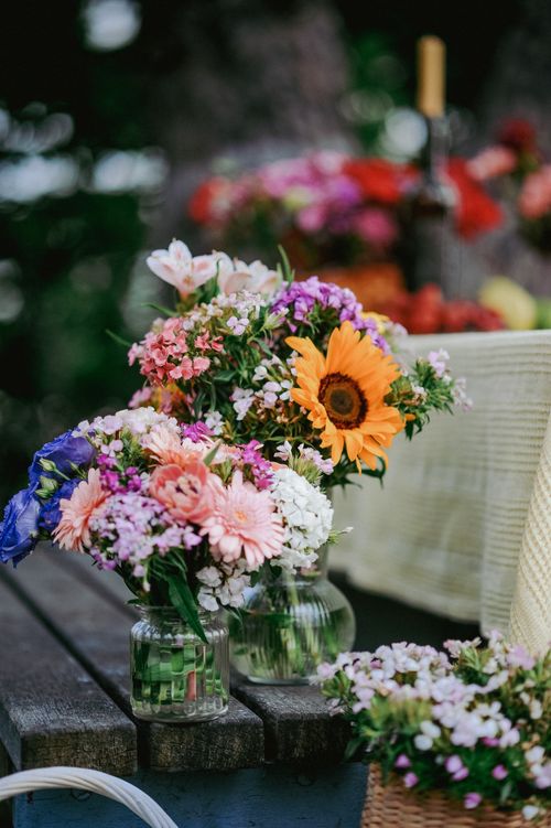 Free A colorful arrangement of summer flowers in glass vases on an outdoor wooden table. Stock Photo