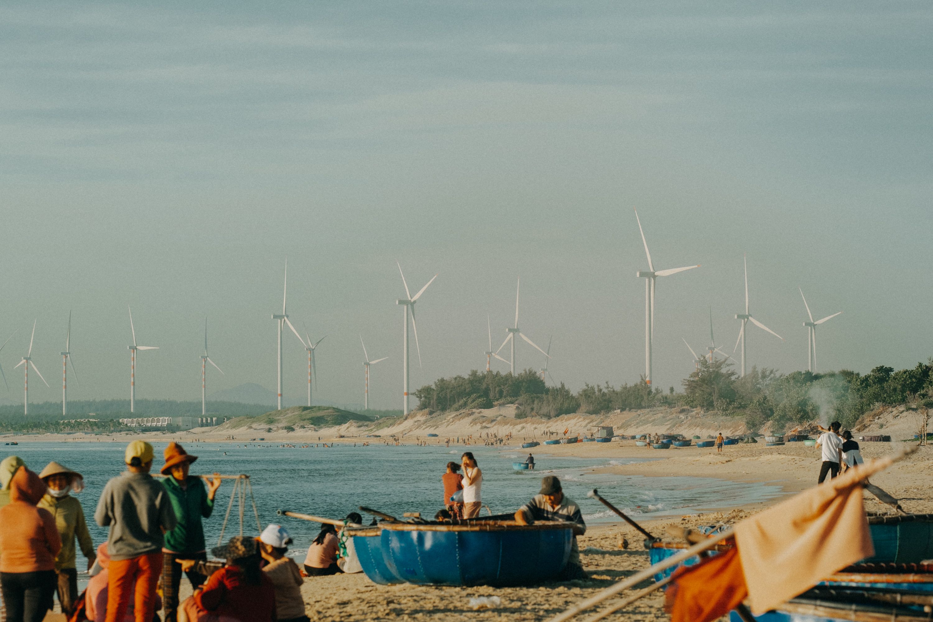 Sunny beach with wind turbines in the background, showcasing sustainable energy and local life.