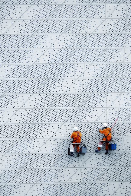 Two workers suspended on a modern building facade performing maintenance tasks.