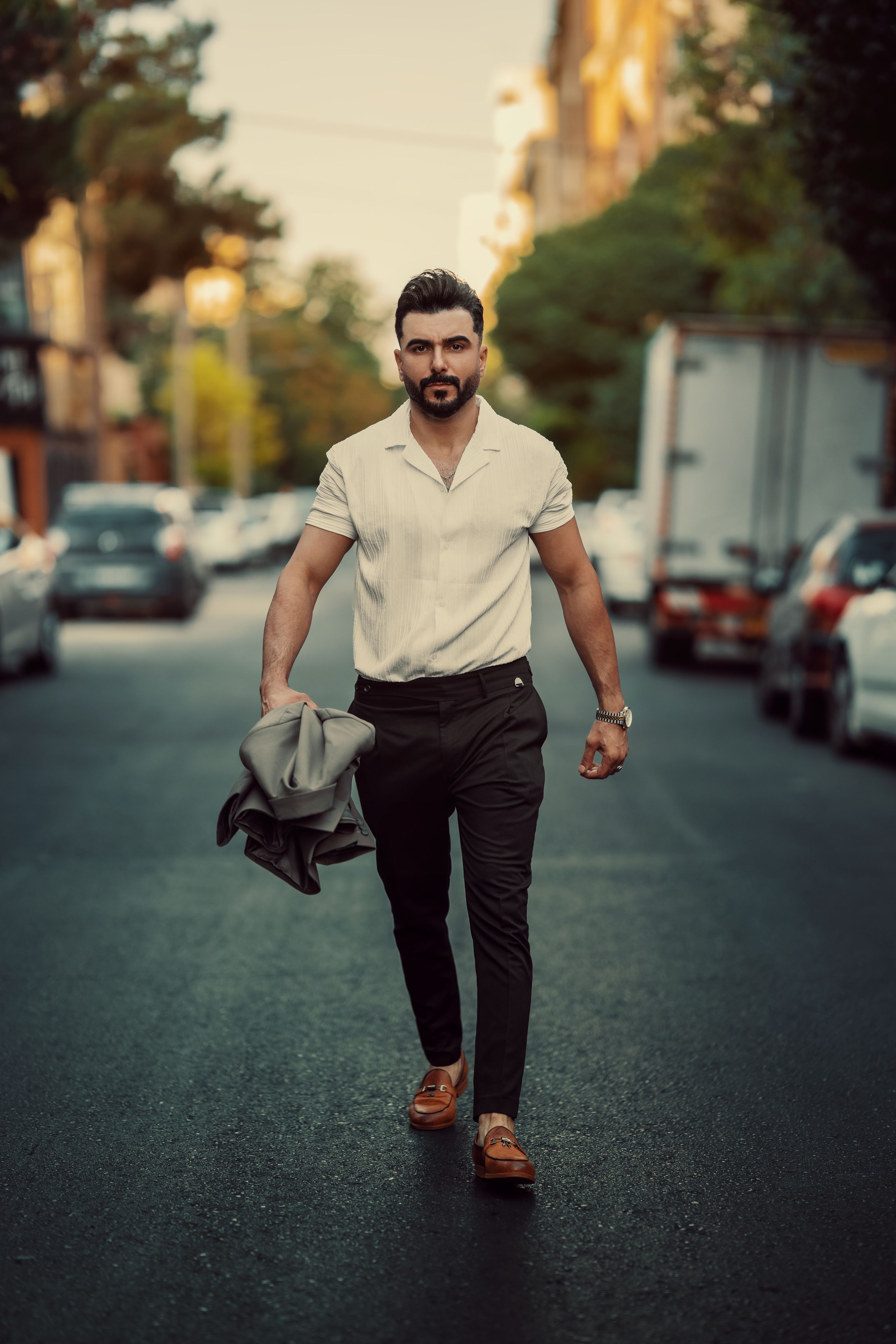 Homem estiloso caminhando confiante pela rua da cidade em uma camisa branca, personificando a moda e a elegância urbana.