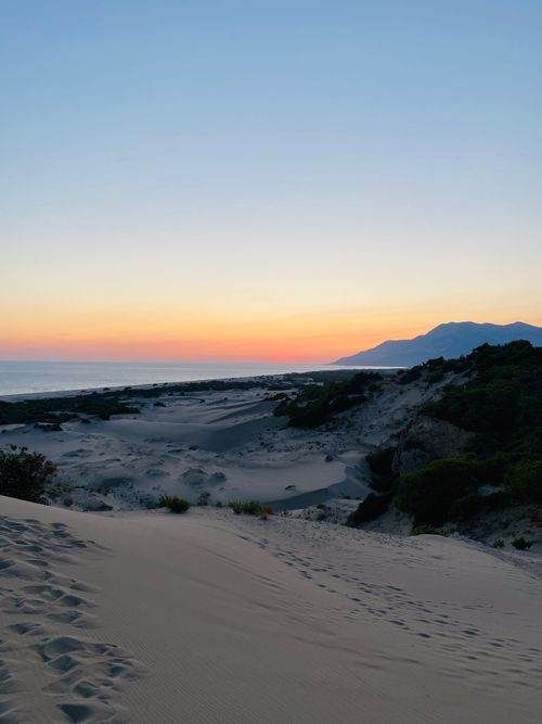 Free A serene landscape of coastal dunes at sunset with mountain backdrop. Stock Photo