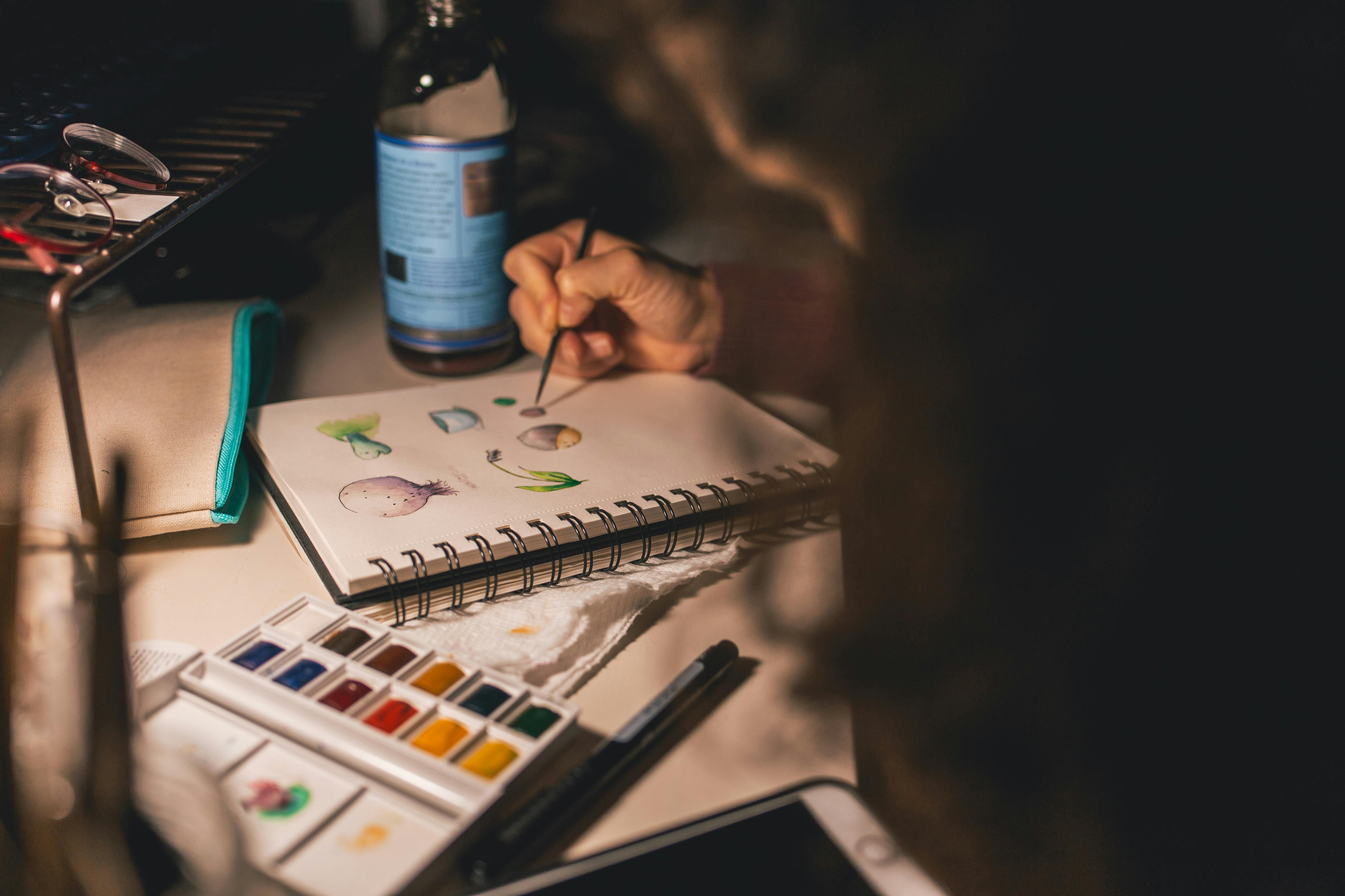 person writing illustration in spiral notebook