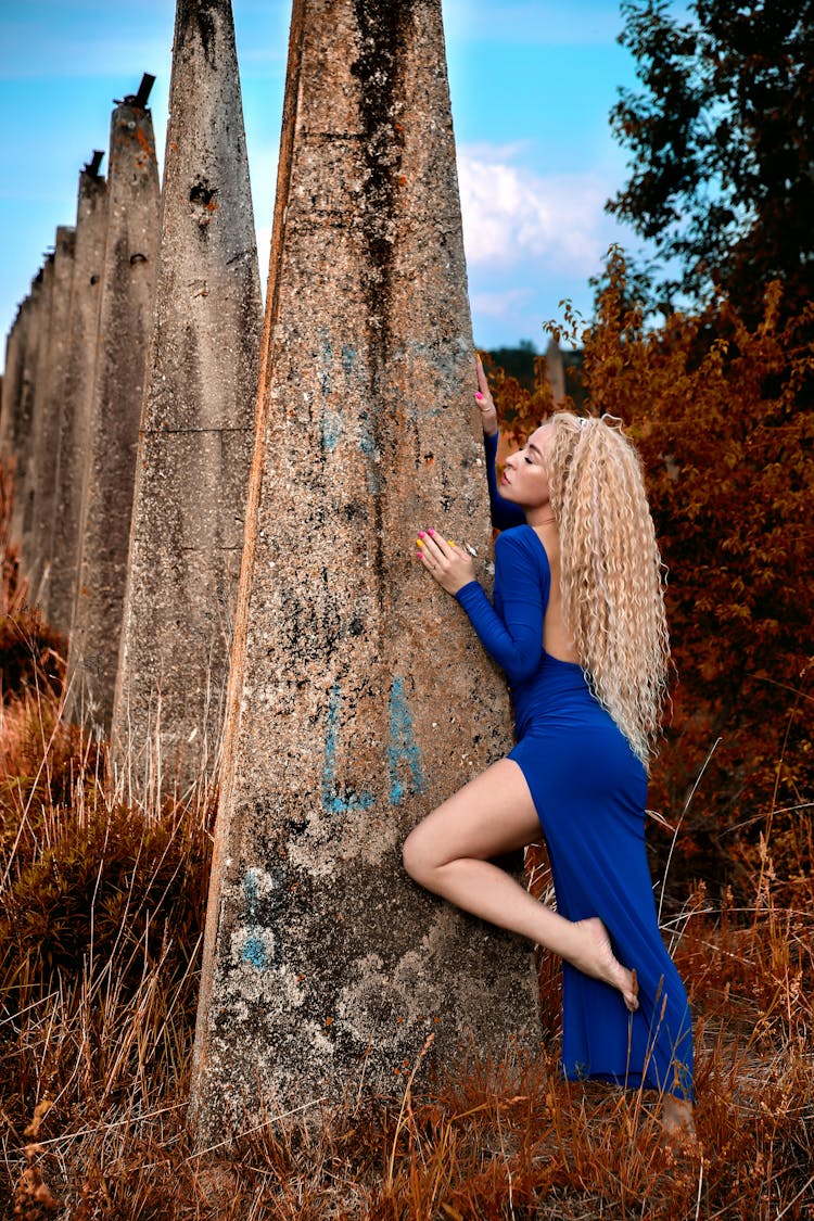 Young Woman In A Dress Posing Next To Large Concrete Poles 