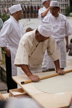 Asian chefs demonstrating traditional dough techniques in an outdoor setting.