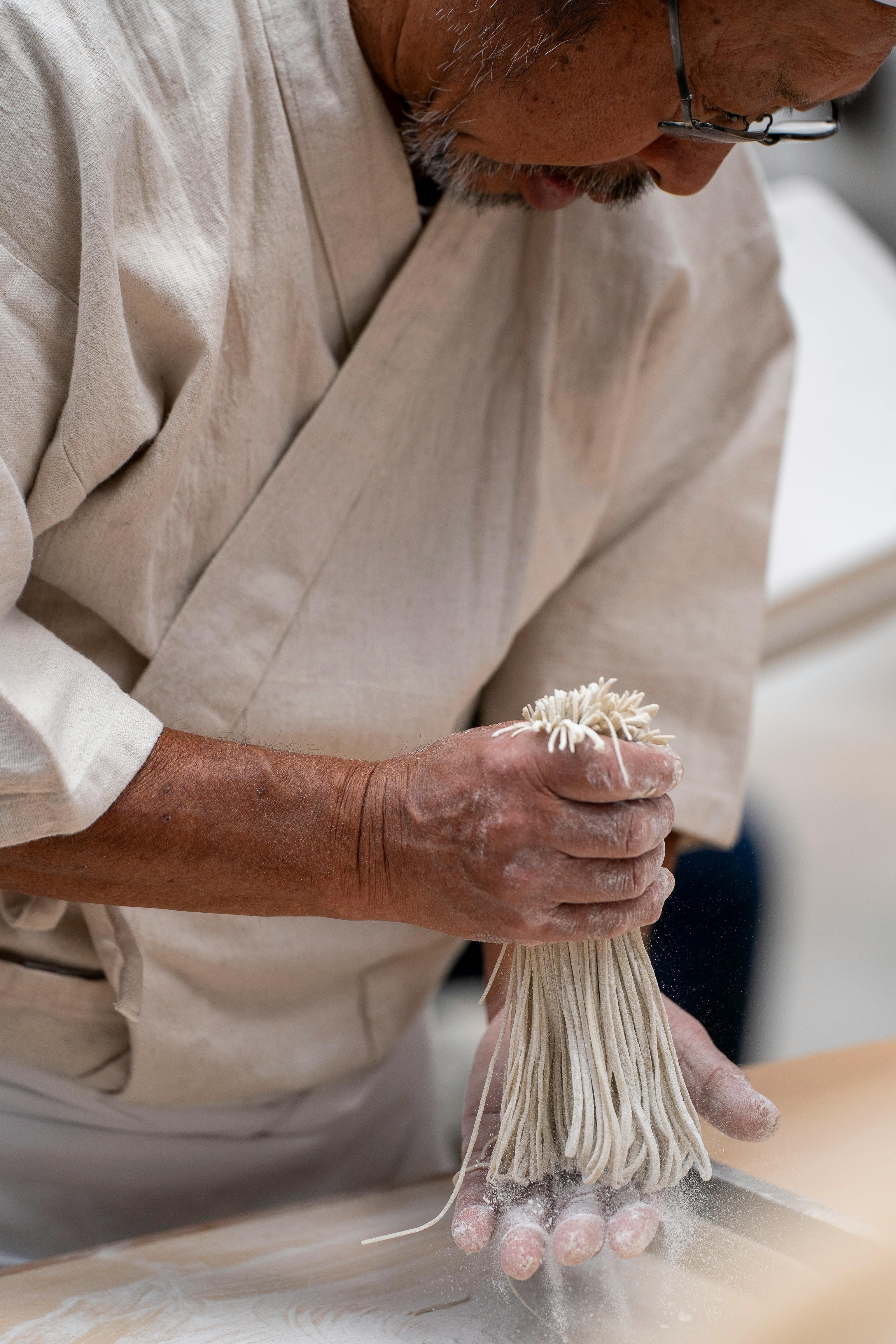 Asian chef skillfully prepares fresh noodles, focusing on traditional techniques and artful craftsmanship.