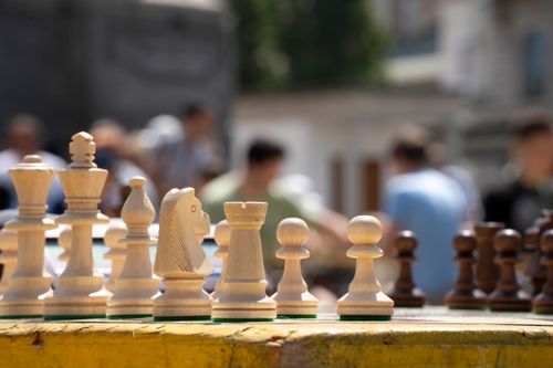 Free Wooden chess pieces on a board outdoors with people blurred in the background. Stock Photo