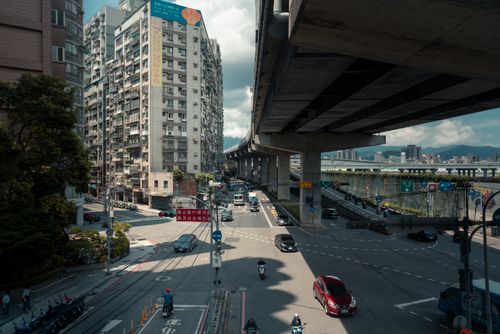 Free View of a bustling city intersection under an elevated highway with cars and motorbikes in motion. Stock Photo