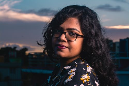 Free A striking portrait of a woman with eyeglasses at twilight, showcasing a vibrant urban background. Stock Photo