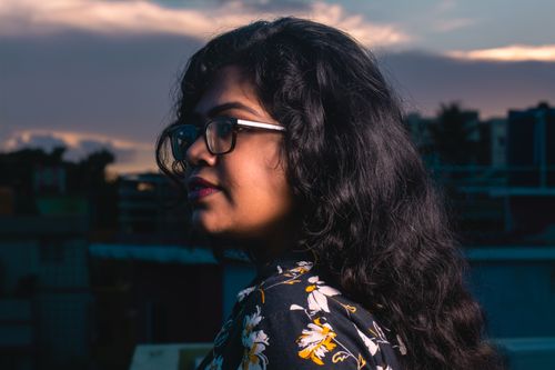 Free A serene portrait of a woman wearing eyeglasses on a rooftop at twilight with a dramatic sky background. Stock Photo