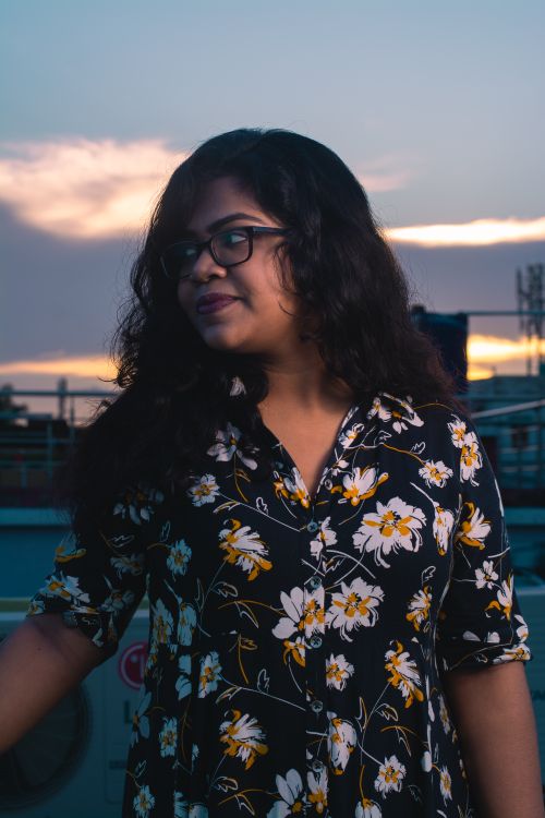 Free A young woman with eyeglasses stands on a rooftop terrace, enjoying the sunset. Stock Photo