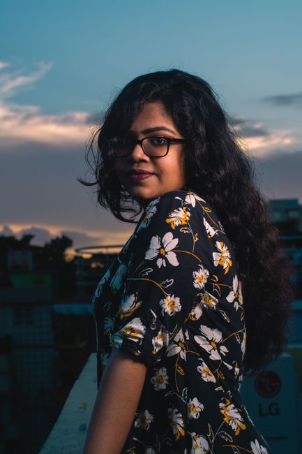 Portrait of a young woman with glasses standing on a city balcony at sunset.