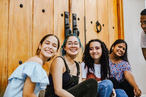 Free A group of young women sitting and smiling in front of wooden doors in an urban setting. Stock Photo