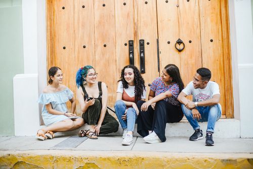 Free A diverse group of friends casually sitting outside large wooden doors, enjoying a sunny day. Stock Photo