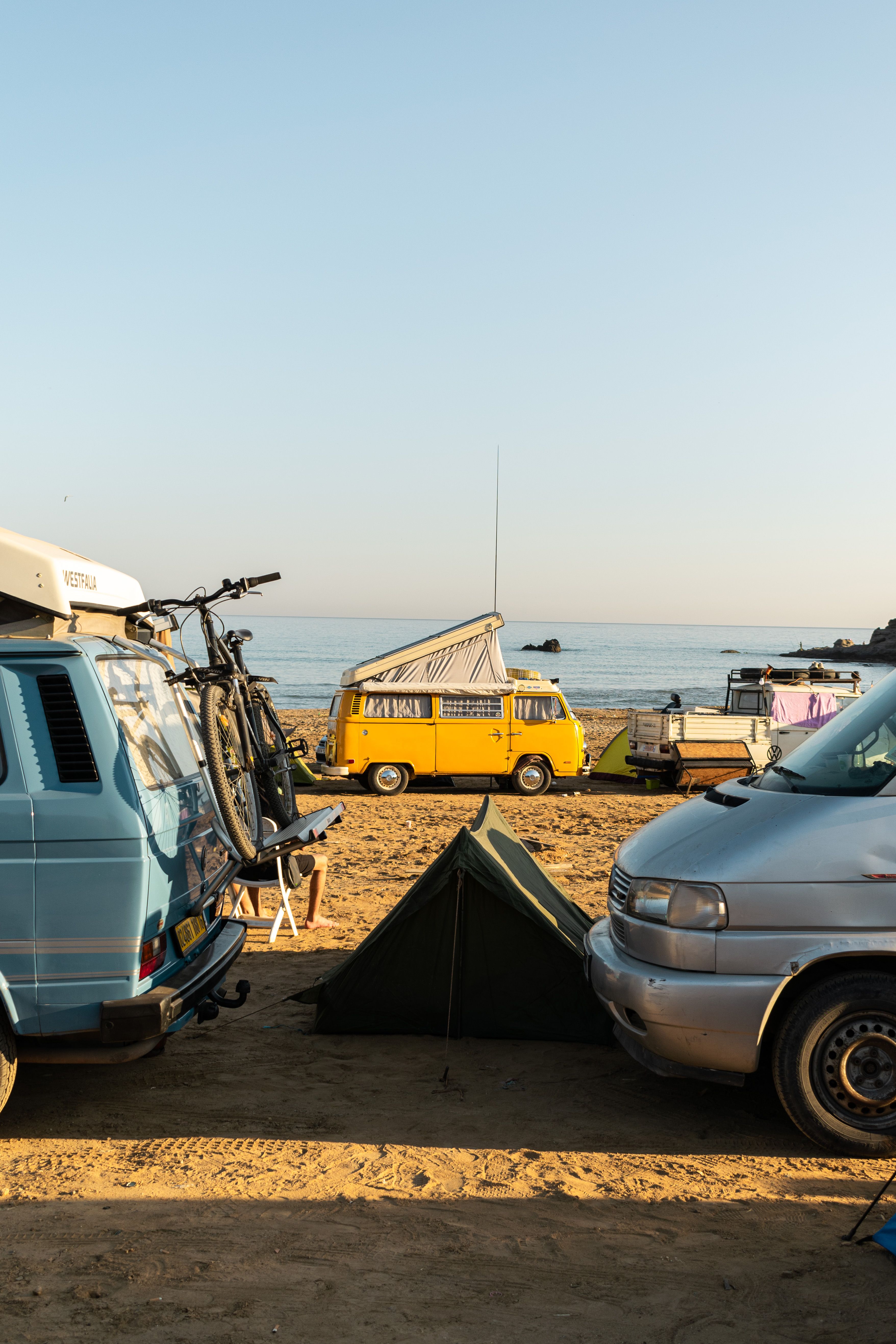 A serene beach camping scene in Boumerdès with vans, tent, and ocean view at daytime.