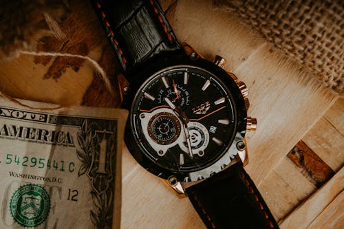 Free Close-up of a luxury wristwatch with a dollar bill on a wooden surface. Stock Photo