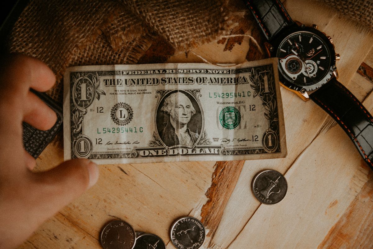 A vintage one-dollar bill surrounded by coins on a wooden tabletop