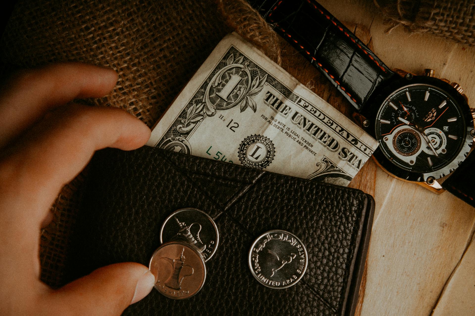 A detailed look at a wallet with money and a watch on a wooden surface.