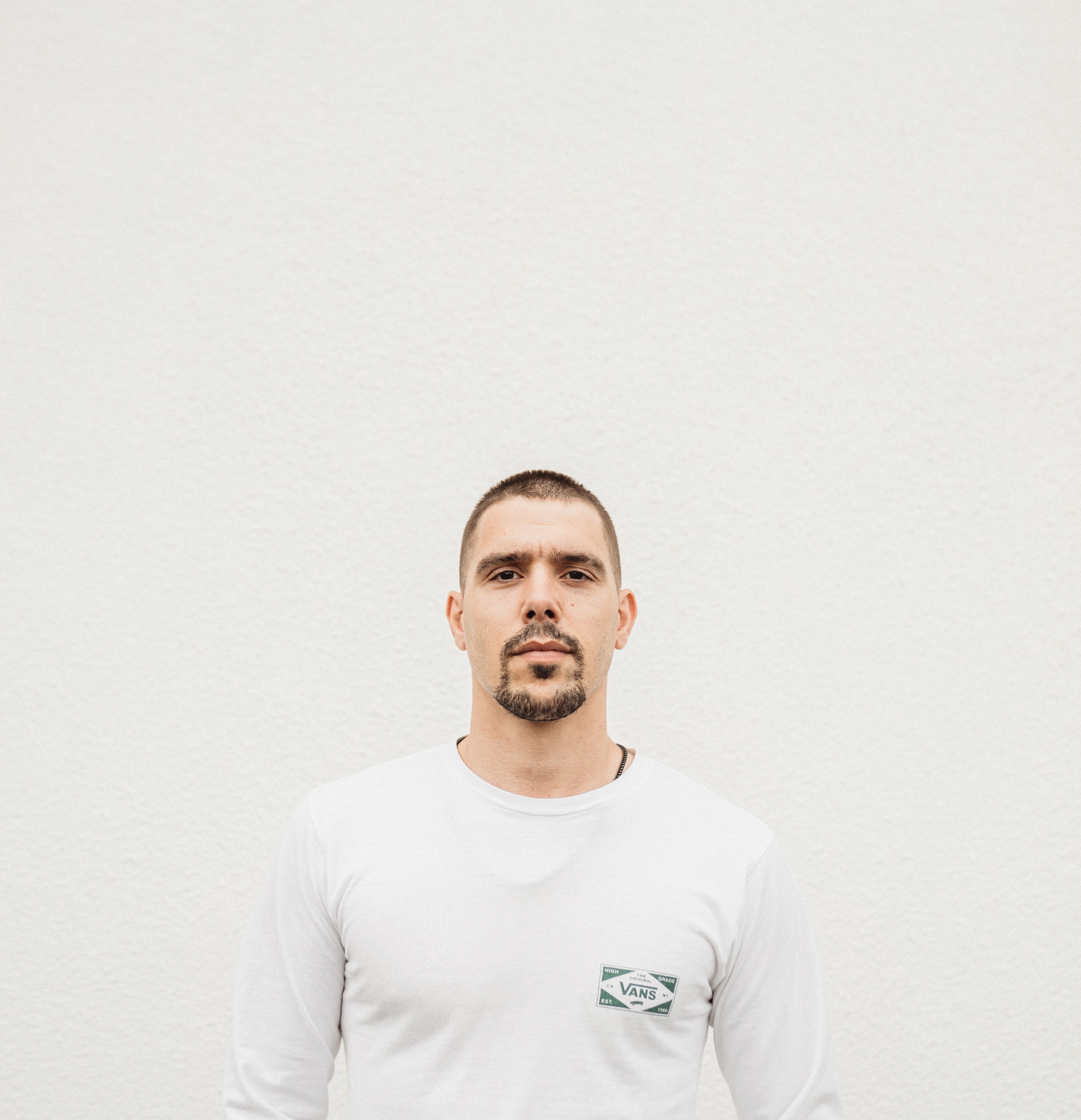 Portrait of a man in a white shirt with a neutral background, showcasing a minimalist aesthetic.