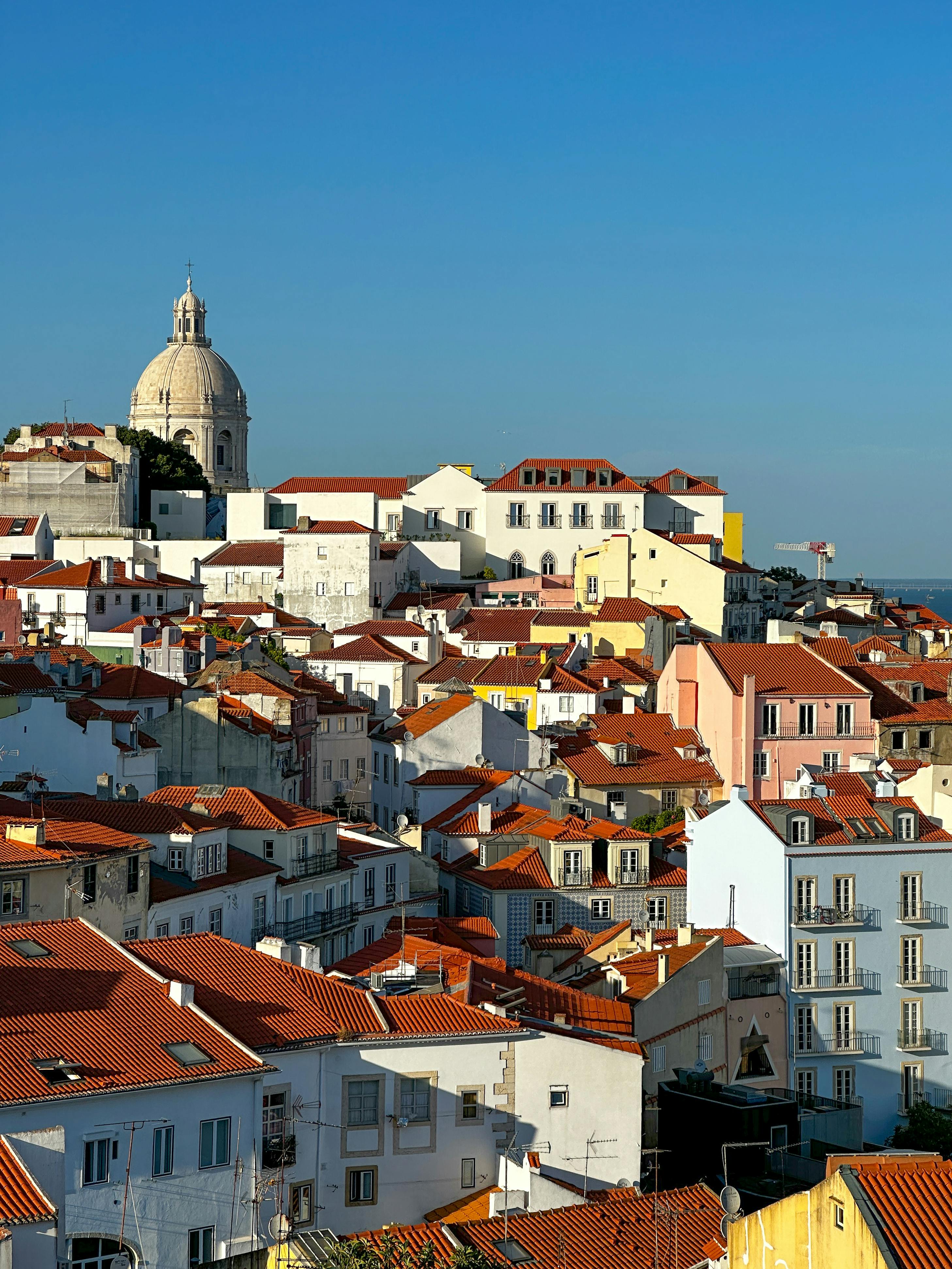 A vibrant, sunlit aerial view of Lisbon's Alfama district showcasing traditional architecture and a prominent dome.