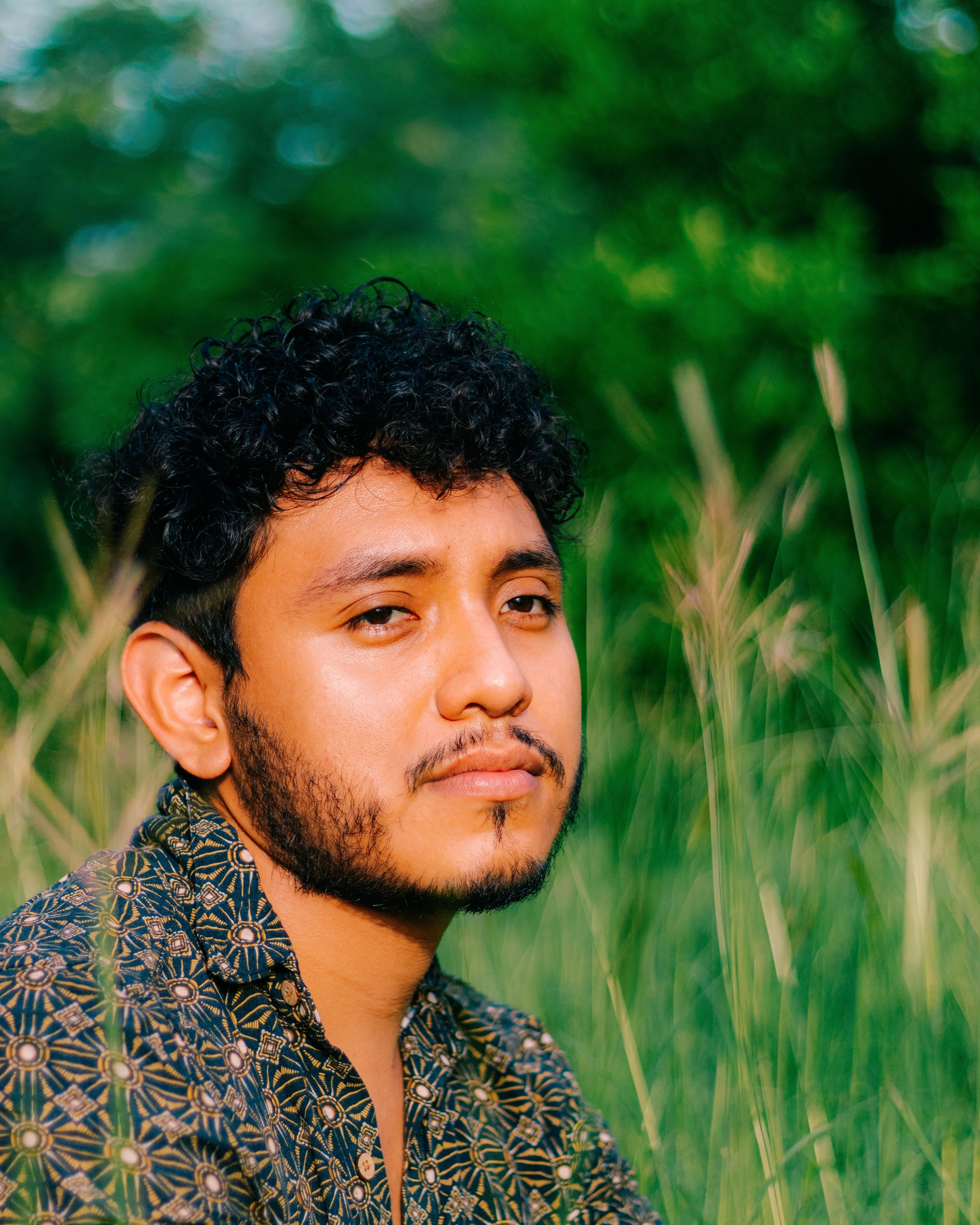 A man with a beard enjoys a tranquil moment in a sunlit meadow, surrounded by greenery.