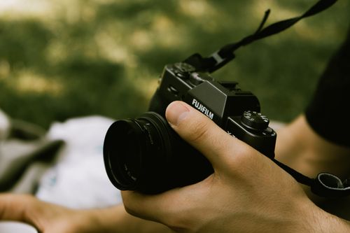 Free A close-up of a person holding a camera outdoors with a blurred natural background. Stock Photo
