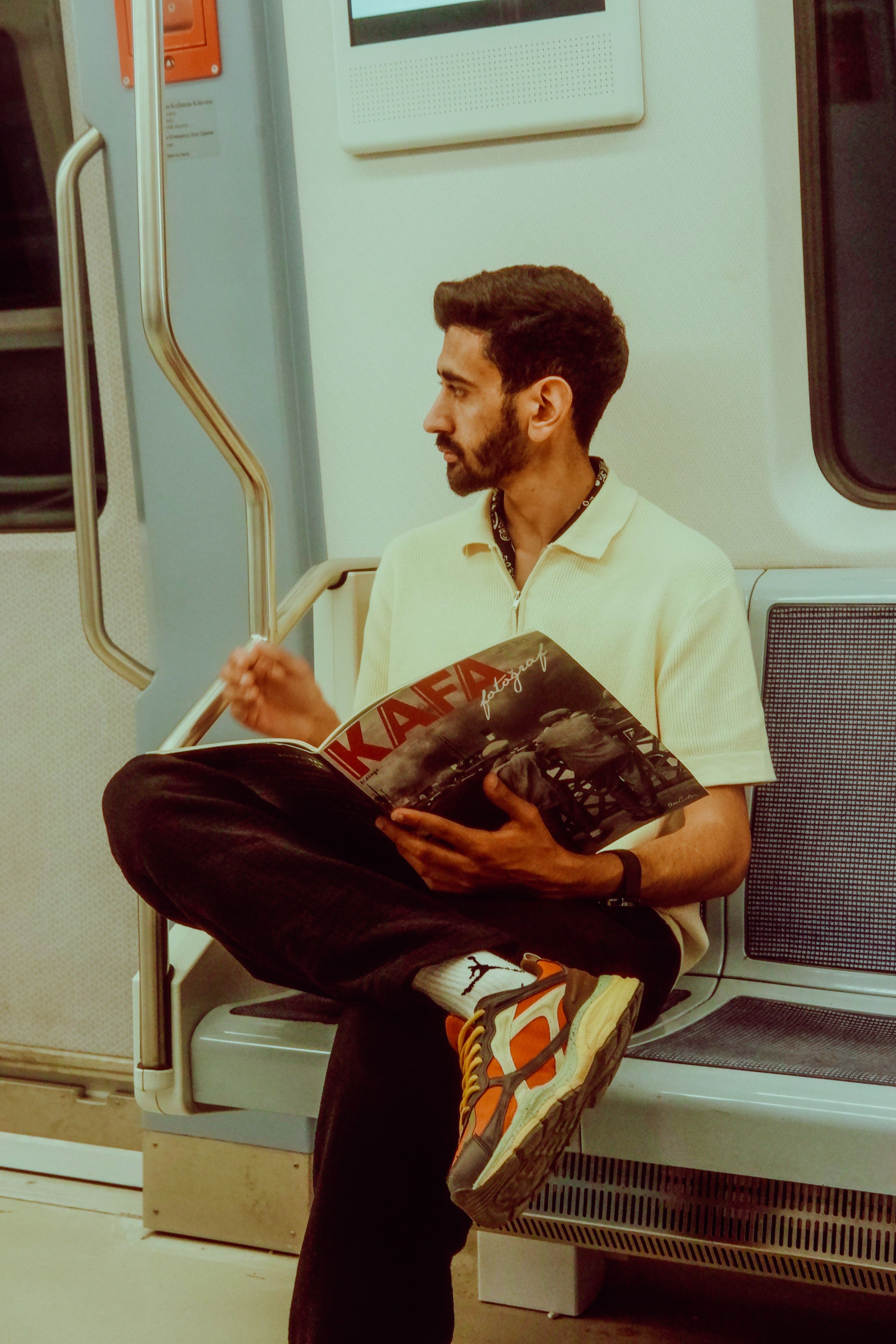 Young man sitting on subway, engaging in magazine reading during commute.