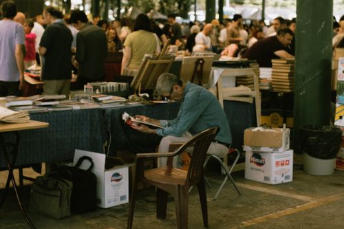 Free Older man reading a magazine at a bustling outdoor book market. Stock Photo