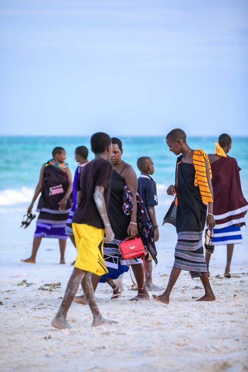 Free Group of people in vibrant attire walking on Zanzibar beach, Tanzania. Stock Photo