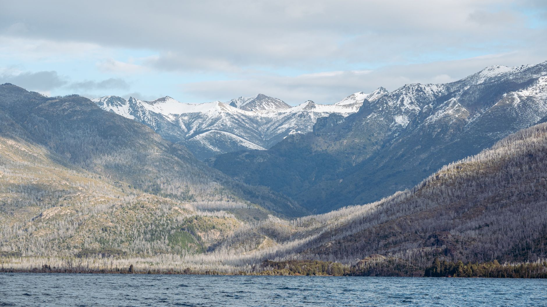 Stunning view of snow-capped mountains and serene lake under a cloudy sky, perfect for nature enthusiasts.