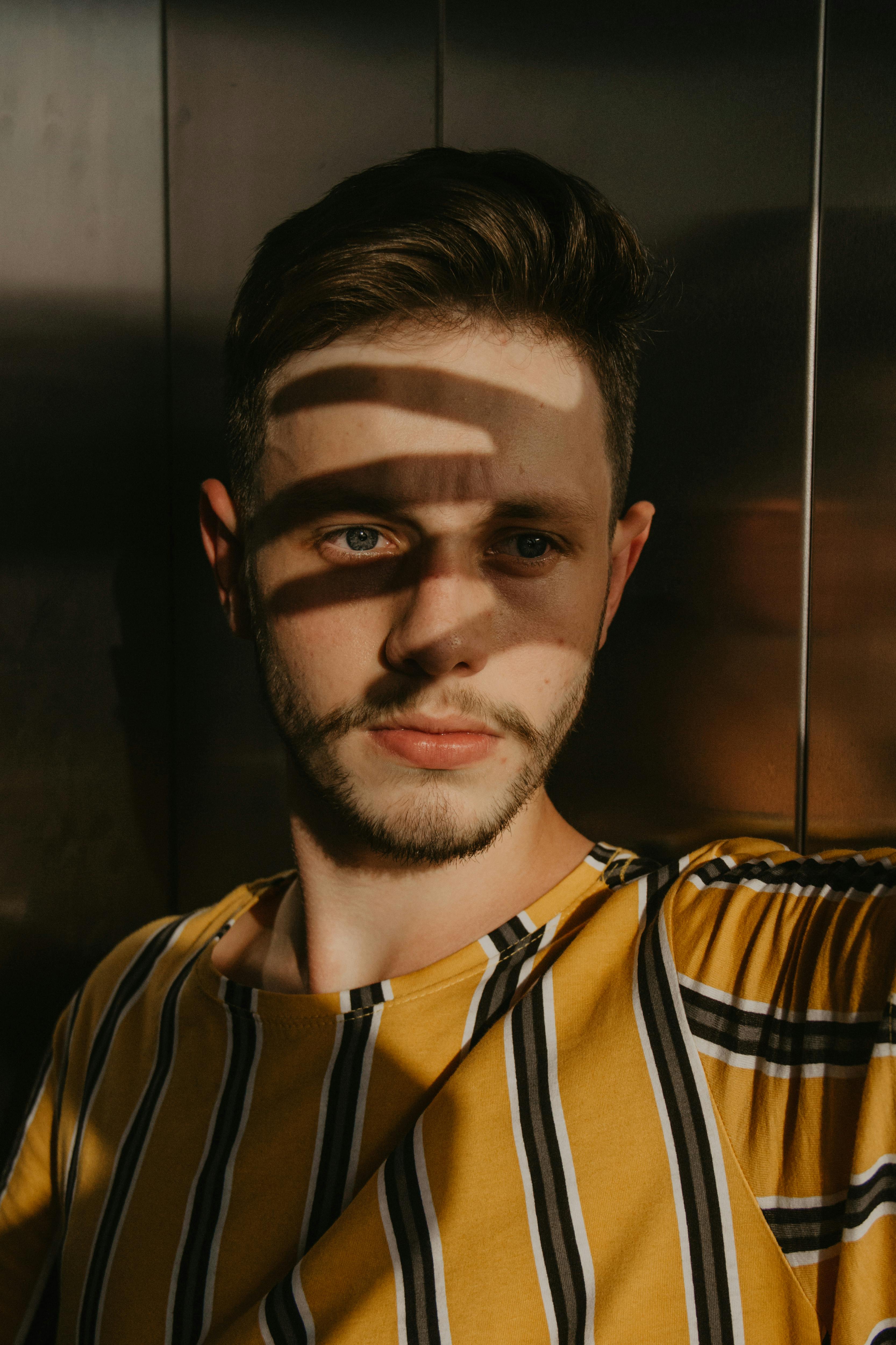 Artistic portrait of a man with shadow patterns on his face, evoking mystery and depth.