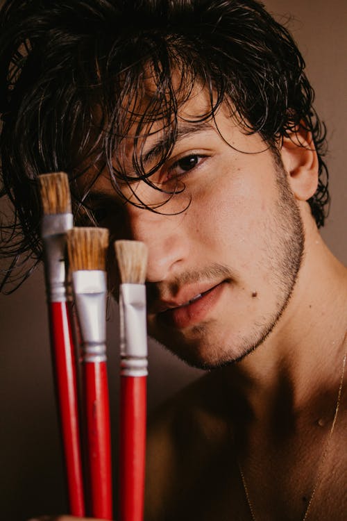 Man Holding Paintbrushes in front of Face