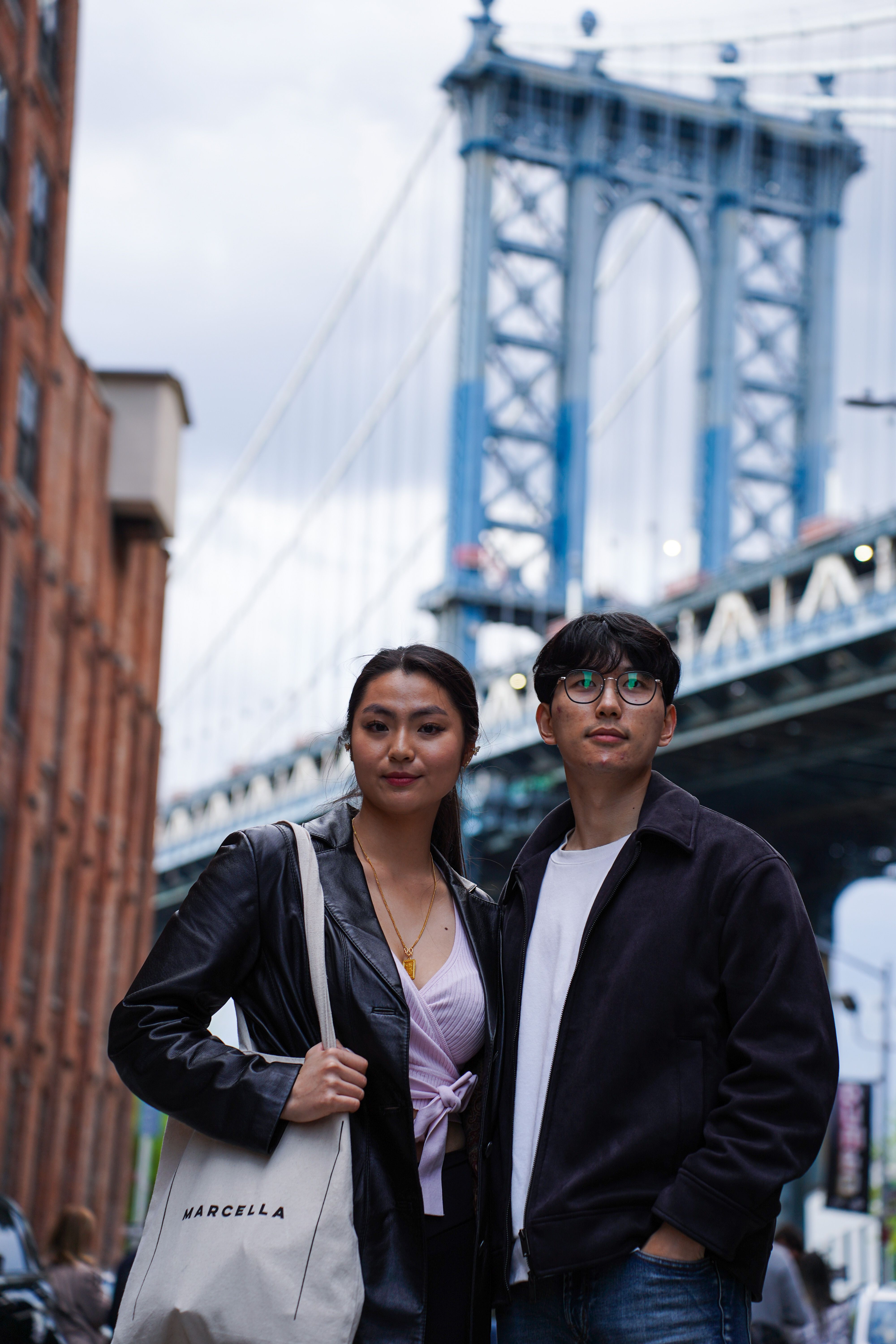 A young couple stands with the iconic Manhattan Bridge in the background, a prominent NYC landmark.